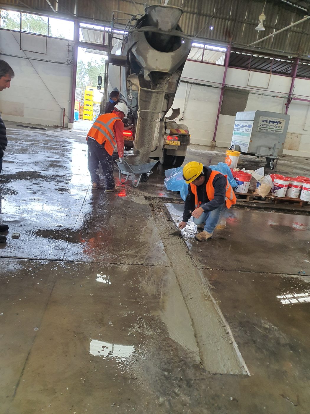 שני עובדים ביישור בטון טרי מול מערבל, בקסדות ואפודים