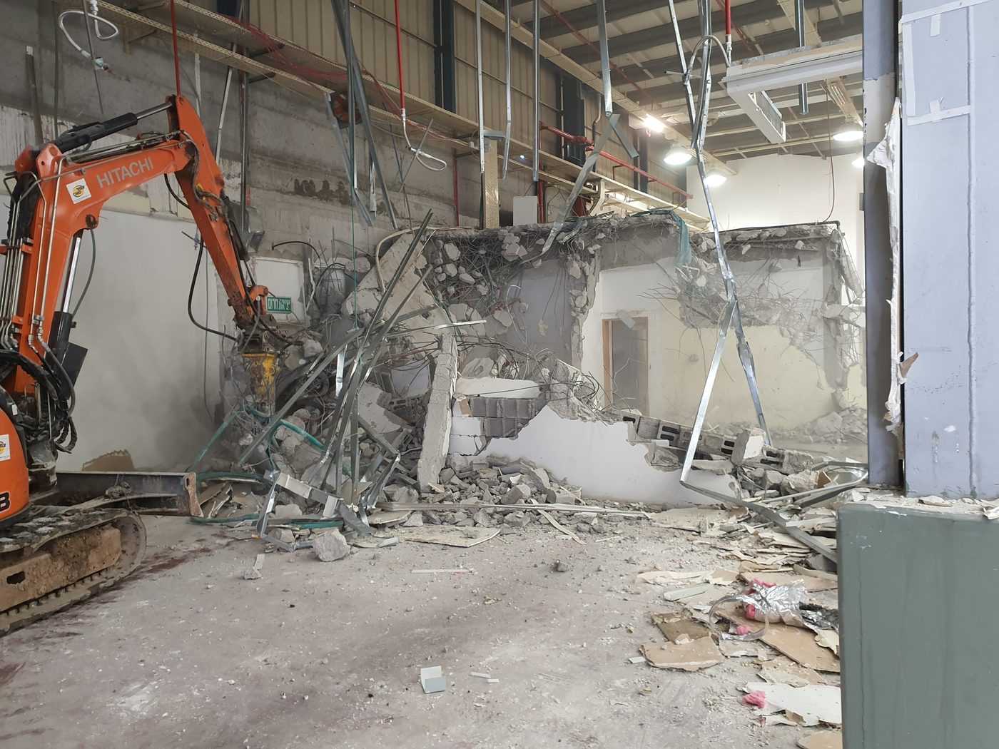 מחפרון עם פטיש הידראולי מפרק קיר בטון במבנה תעשייה, זיון חשוף