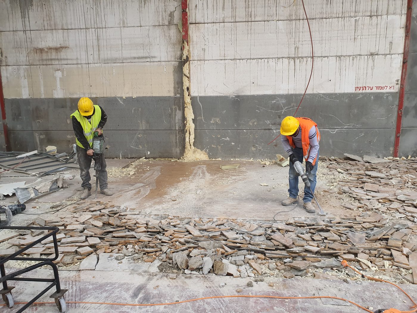 שני עובדים חוצבים תעלות בקיר בטון, בקסדות ואפודים